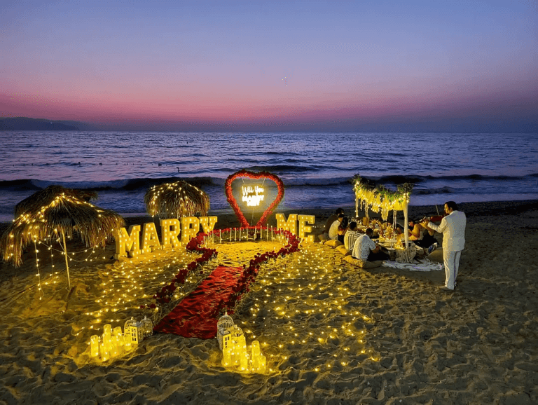 Gün batımında kumsalda ışıklı Marry Me ve kırmızı halı