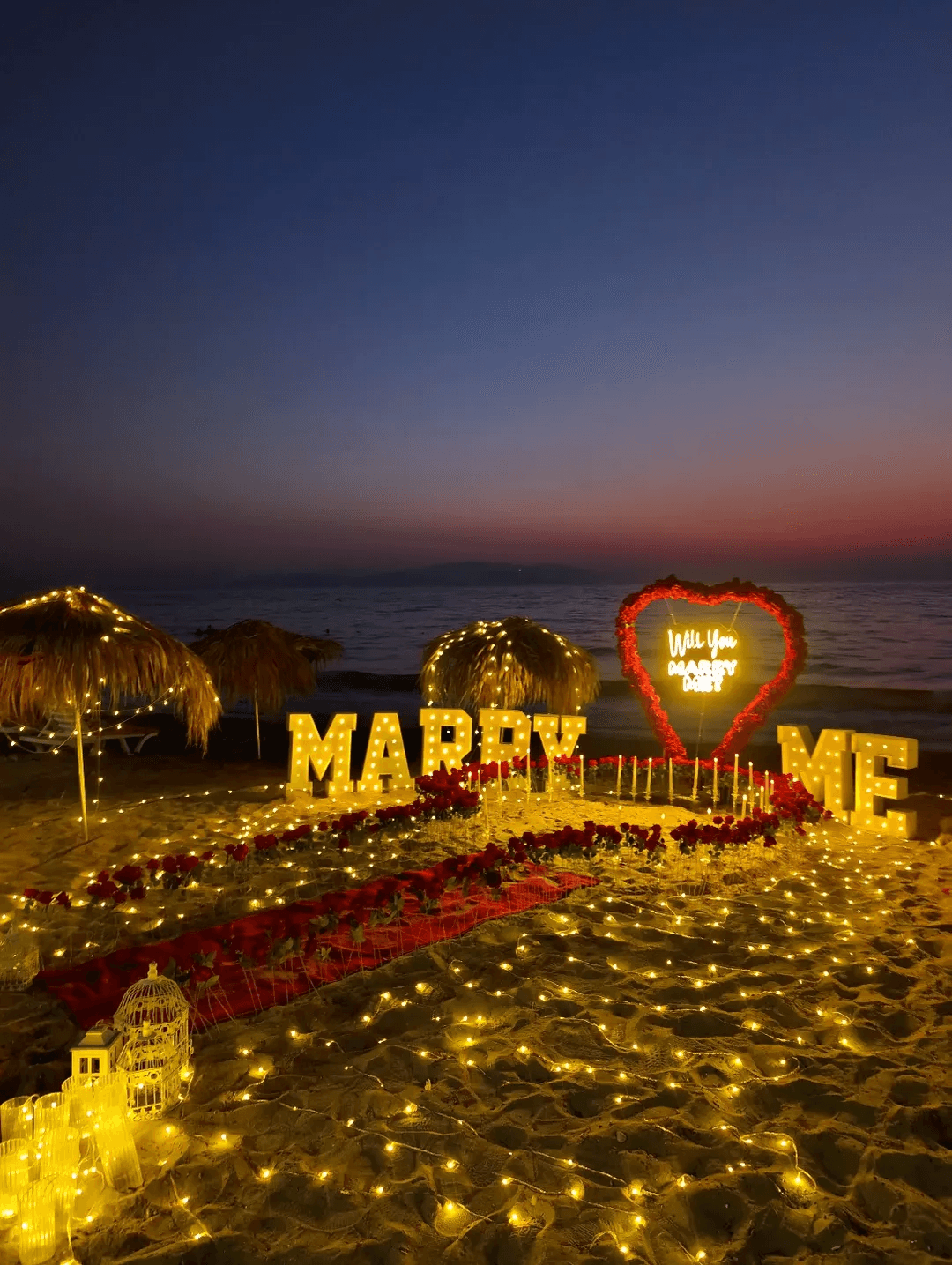 Gün batımında ışıklı Marry Me harfleri ve kalple evlilik teklifi